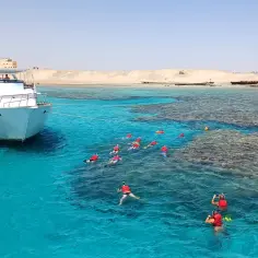 Grupa turystów w kamizelkach ratunkowych snorkeluje w krystalicznie czystej wodzie. Statek cumuje obok. To wspaniałe marsa alam atrakcje.