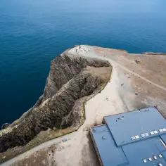 Widok z lotu ptaka na klifowe wybrzeże i budynek turystyczny na Nordkapp. Ludzie spacerują po ścieżkach, podziwiając ocean.