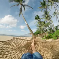 Nogi w hamaku na plaży, palmy i ocean. Idealne miejsce na wakacje w listopadzie, gdzie najcieplej.