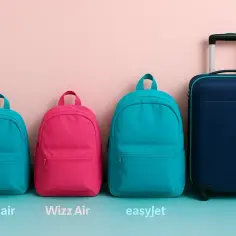Trzy plecaki (niebieski, różowy, niebieski) i granatowa walizka LOT na tle różowej ściany.
