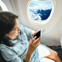 Kobieta z telefonem w ręku, siedząca przy oknie w samolocie Ryanair. Widok na chmury z góry.