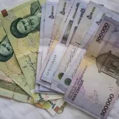 Kupka banknotów, w tym waluta Iranu, z wizerunkami przywódców i budynków.