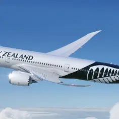 Boeing 787 Air New Zealand z charakterystycznym czarnym malowaniem z liściem paproci na ogonie, lecący na tle błękitnego nieba i chmur.