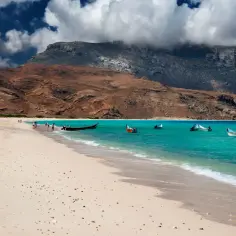 Piękna plaża na Sokotrze, idealna na wycieczkę. Turkusowa woda, łodzie i górzysty krajobraz tworzą niezapomniany widok.