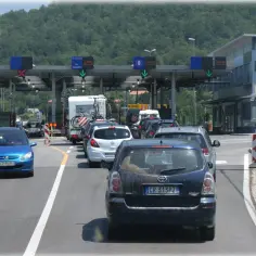 Korki na granicy, kierowcy czekają na zakup winiet do Chorwacji. W tle budynki przejścia granicznego i zielone wzgórza.