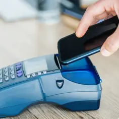 Dłoń zbliża smartfon do terminala płatniczego. Szybka płatność zbliżeniowa, bez konieczności podawania PIN-u, nawet za transakcje powyżej limitu bezgotówkowego.