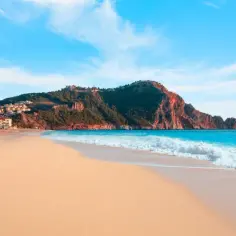 Plaża Kleopatry w Alanyi, Turcja. Złoty piasek, turkusowe morze i skaliste wzgórze z zamkiem na horyzoncie.