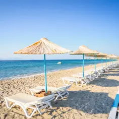 Słoneczna plaża na wyspie Kos, z rzędem leżaków i parasoli. Błękitne morze i niebo tworzą idealne tło dla wakacyjnego wypoczynku.
