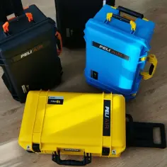 Trzy walizki Peli Air w kolorach: żółtym, niebieskim i czarnym, stojące na drewnianej podłodze.