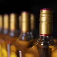 Rząd butelek alkoholu z złotymi zakrętkami na ciemnym tle.