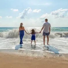 Rodzina na plaży, fale rozbijają się o brzeg. Idealny widok, gdy zastanawiasz się, co zabrać na wakacje nad morze z dzieckiem.
