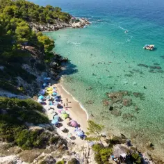 Słoneczna plaża na Sithonii, pełna kolorowych parasoli i kąpiących się ludzi w krystalicznie czystej wodzie.