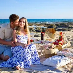Romantyczny piknik na plaży w Protaras na Cyprze. Para cieszy się chwilą przy winie i owocach, z morzem w tle.