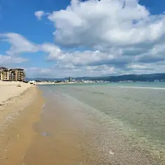 Piękny, słoneczny brzeg z piaszczystą plażą, turkusową wodą i budynkami w oddali. Idealne miejsce na wakacje.