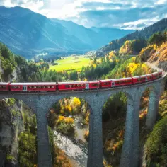 Czerwony pociąg Bernina Express przemierza malowniczy most nad doliną w jesiennych barwach. Sprawdź bernina express cena i zaplanuj podróż!
