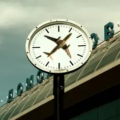 Zegar z samolotem na tle lotniska. Pytanie "ile wczesniej byc na lotnisku" nabiera tu nowego znaczenia.