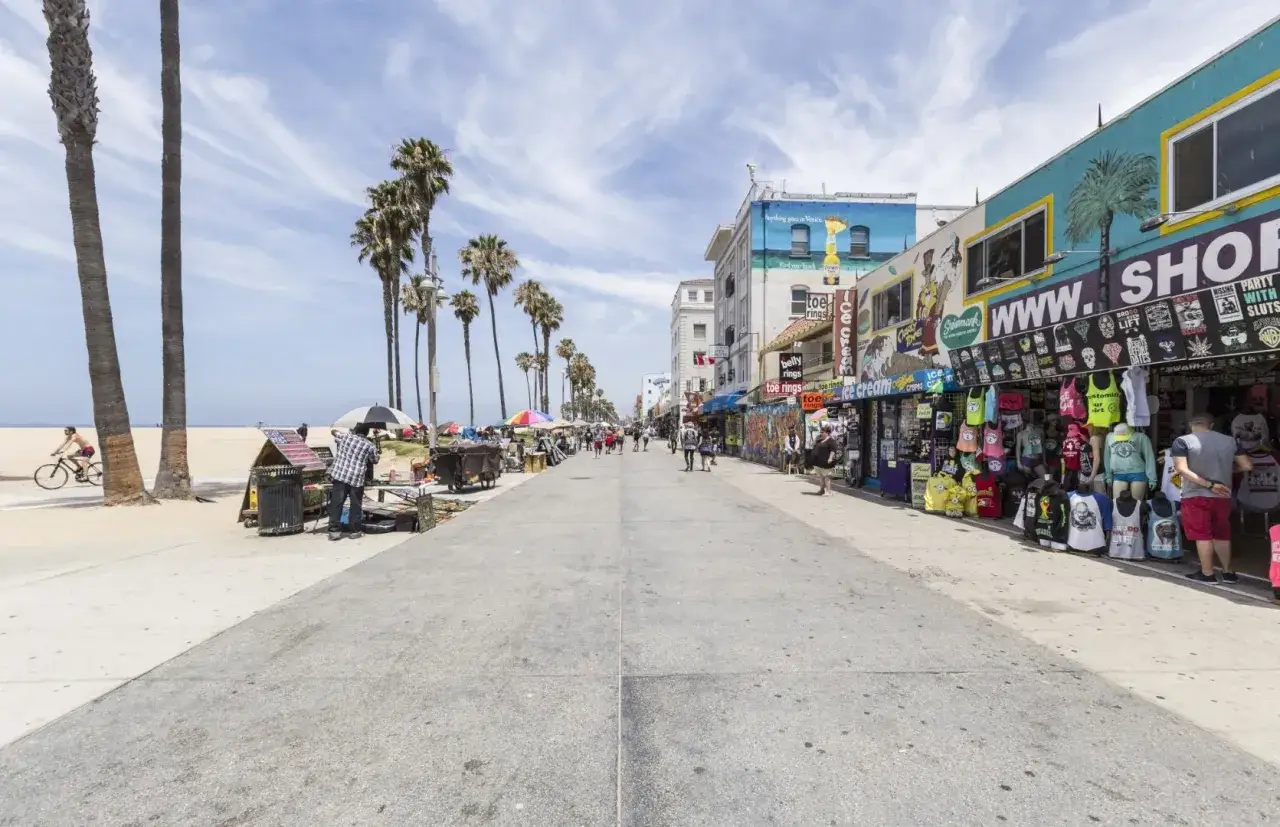 Tętniący życiem deptak w Venice Beach z palmami, sklepikami z pamiątkami i ludźmi spacerującymi w słoneczny dzień.
