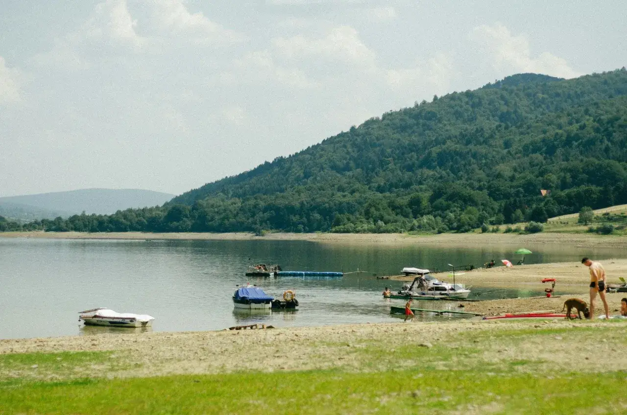 Słoneczne wakacje w Polsce nad jeziorem. Łodzie, plażowicze i zielone wzgórza tworzą idylliczny krajobraz.