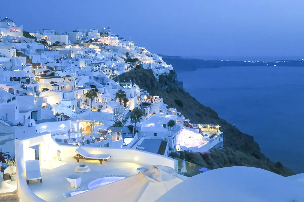 Białe domy na klifie Santorini, morze i światła miasta. Idealne miejsce na tanie wakacje w Grecji.