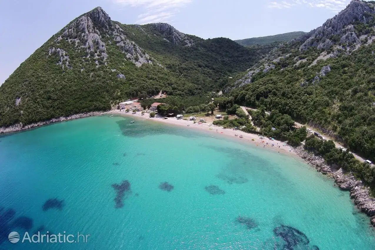 Malownicza zatoka z turkusową wodą na półwyspie Pelješac. Plaża z kilkoma budynkami i ludźmi, otoczona zielonymi wzgórzami.