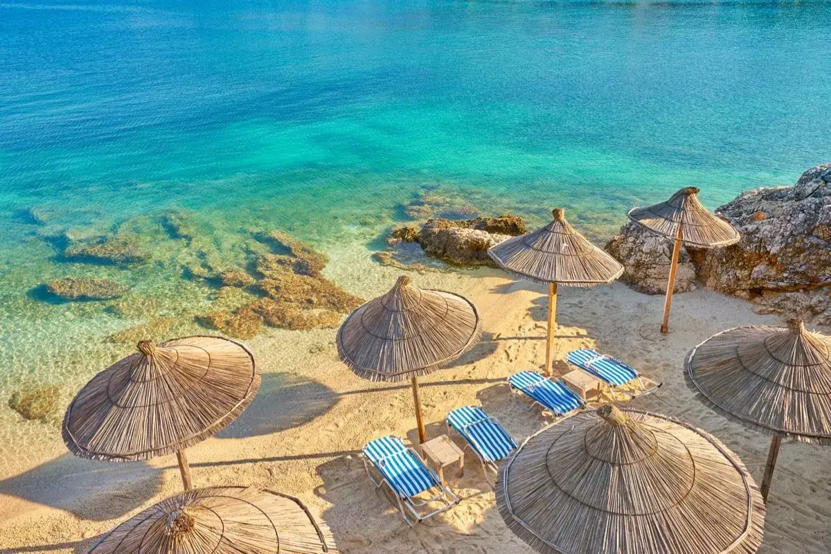 Albania, czerwiec: słoneczna pogoda na plaży z leżakami i parasolami. Turkusowa woda i złoty piasek zapraszają do relaksu.