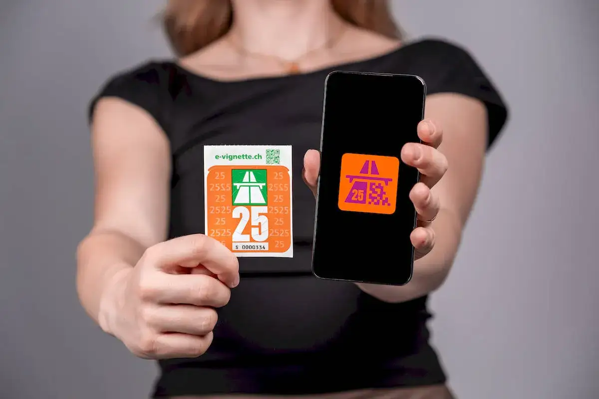 Ręce trzymają naklejkę i smartfon z aplikacją. Na naklejce widnieje napis