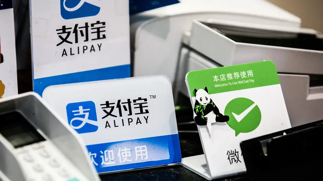 Znaki Alipay i WeChat Pay, popularne formy płatności w Chinach, na tle terminali płatniczych.