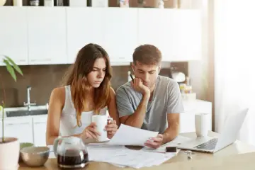 Para zmartwiona analizuje dokumenty, szukając wsparcia. Uniqa assistance może pomóc w trudnych sytuacjach.