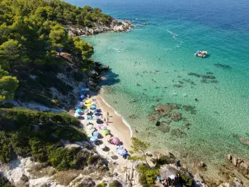 Słoneczna plaża na Sithonii, pełna kolorowych parasoli i kąpiących się ludzi w krystalicznie czystej wodzie.